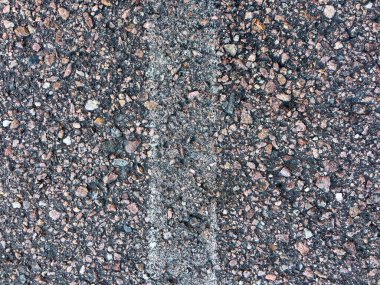 Soluk beyaz çizgi işaretli asfalt bir yol yüzeyine yakın çekim. Asfaltın kaba dokusu, içine yerleştirilmiş küçük taşlar ve çakıl taşlarının karışımı ile vurgulanır ve aşınma izleri gösterir.