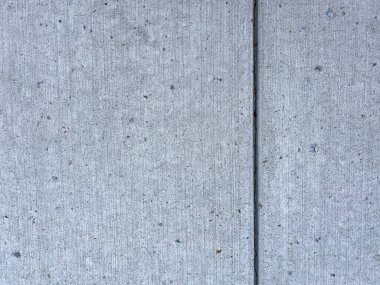 İki bölümün birleştiği yere odaklanmış beton kaldırımın detaylı bir yakın çekimi. Açık gri beton, küçük gömülü taşlar ve parçacıklardan oluşan ince bir doku sergiliyor. Soluk dikey