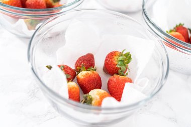 Parlak kırmızı çilekler, küf izleriyle karışmış, beyaz peçetedeki kağıt havluyla kaplı cam bir kasede dinleniyor, depolama tekniklerini gösteriyor..