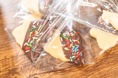 Dikkatlice paketlenmiş Noel kurabiyeleri, çikolataya batırılmış ve şeffaf selofan ambalajla sunulmuş, bayram hediyesi olarak mükemmel..