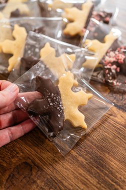 Dikkatlice paketlenmiş Noel kurabiyeleri, çikolataya batırılmış ve şeffaf selofan ambalajla sunulmuş, bayram hediyesi olarak mükemmel..