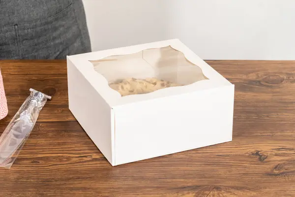 stock image Carefully placing the gingerbread bundt cake, adorned with salted caramel frosting and gingerbread sprinkles, into a white paper bundt cake box with a clear window for gifting.