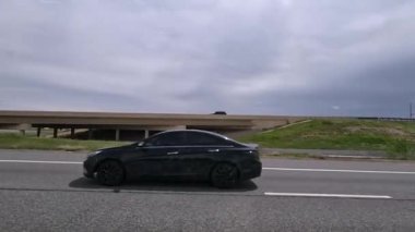 Denver, Colorado, ABD-11 Mayıs 2024-Ağır çekim-A sahnesi Denver, Colorado 'daki I-25 karayolundan beyaz bir SUV ve gümüş bir sedan dahil hareket halindeki araçları yakalıyor. Arkaplan özellikleri ofisi