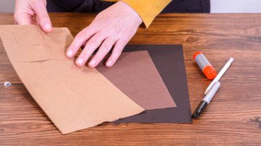 Adım adım. Öğretmen, kahverengi bir çantadan kağıt bir kukla yaparak, çalışma alanı olarak ahşap bir yüzey kullanarak çevrimiçi sınıfa rehberlik ediyor..