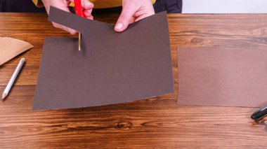 Adım adım. Öğretmen, kahverengi bir çantadan kağıt bir kukla yaparak, çalışma alanı olarak ahşap bir yüzey kullanarak çevrimiçi sınıfa rehberlik ediyor..