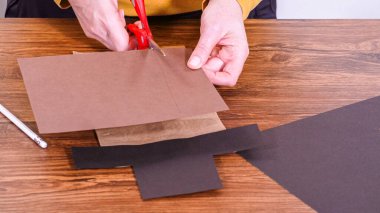 Adım adım. Öğretmen, kahverengi bir çantadan kağıt bir kukla yaparak, çalışma alanı olarak ahşap bir yüzey kullanarak çevrimiçi sınıfa rehberlik ediyor..