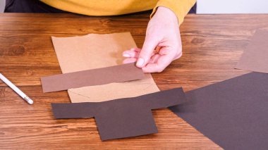 Adım adım. Öğretmen, kahverengi bir çantadan kağıt bir kukla yaparak, çalışma alanı olarak ahşap bir yüzey kullanarak çevrimiçi sınıfa rehberlik ediyor..