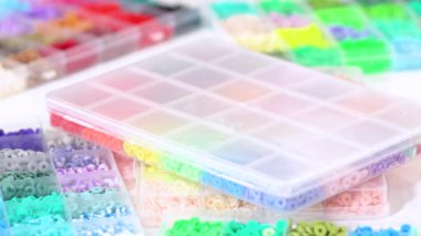 Parlak renkli balçık boncuklarından oluşan geniş bir koleksiyonu bölümlere ayıran eller, karmaşık malzemelerin güzelliğini ve çeşitliliğini vurguluyor.