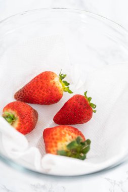 Parlak kırmızı çilekler, küf izleriyle karışmış, beyaz peçetedeki kağıt havluyla kaplı cam bir kasede dinleniyor, depolama tekniklerini gösteriyor..