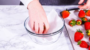 Çilekler, yeni yıkanmış ve kurutulmuş, cam bir kasede güzelce depolanmış kağıt havluyla kaplanmış ve tazeliği korumak için plastikle kaplanmış..