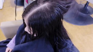 Nazik eller saç kurutma makinesini yeni kesilmiş genç bir kızın üzerinden geçirir ve titiz bir şekilde kestikten sonra kurutma işlemini gösterir. Kurutucunun sıcaklığı onun kilitlerine hayat veriyor.