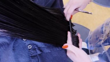 Salonun hareketli atmosferinde, küçük bir kız sabırla oturur. Cilalı kırmızı tırnakları nemli saçlarını dikkatlice kesen bir stilist gibi. Makas parıltısı ve hassas el hareketleri yakalar.