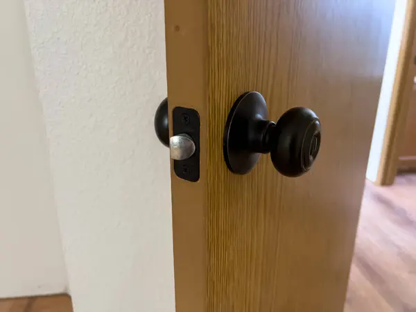 stock image A detailed close-up image of a newly installed black door handle and latch on a wooden door. The door is slightly ajar, revealing the smooth wooden surface and the latch mechanism. The background