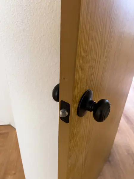 stock image A detailed close-up image of a newly installed black door handle and latch on a wooden door. The door is slightly ajar, revealing the smooth wooden surface and the latch mechanism. The background