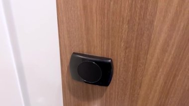 Bu görüntü, ahşap bir otel odasının kapısındaki siyah elektronik kapının detaylı bir yakın çekimini çeker. Çağdaş otel tasarımında kullanılan güvenlik özelliklerini vurgular..