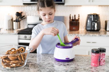 Odaklanmış bir dikkatle, bu filizlenen aşçılık sanatçısı krakerleri erimiş çikolataya batırarak iyi aydınlatılmış bir ev mutfağının sıcaklığında tatlı tatlar yaratıyor..