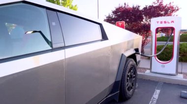 Santa Fe, New Mexico, ABD-31 Mayıs 2024-Slow motion-A Tesla Cybertruck açık hava şarj istasyonundaki bir Tesla Supercharger 'a bağlı. Siber kamyonun parlak, açısal tasarımı...