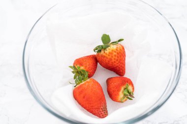 Parlak kırmızı çilekler, küf izleriyle karışmış, beyaz peçetedeki kağıt havluyla kaplı cam bir kasede dinleniyor, depolama tekniklerini gösteriyor..