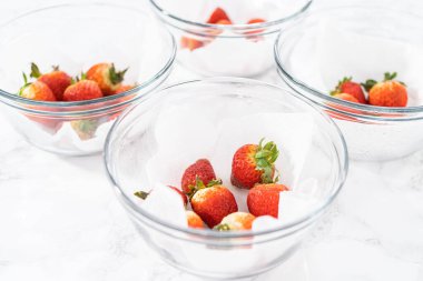 Parlak kırmızı çilekler, küf izleriyle karışmış, beyaz peçetedeki kağıt havluyla kaplı cam bir kasede dinleniyor, depolama tekniklerini gösteriyor..