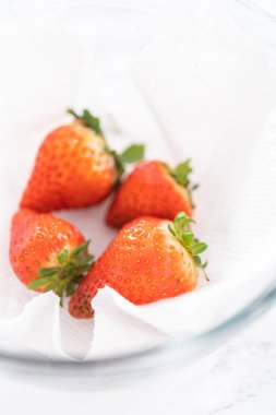 Parlak kırmızı çilekler, küf izleriyle karışmış, beyaz peçetedeki kağıt havluyla kaplı cam bir kasede dinleniyor, depolama tekniklerini gösteriyor..