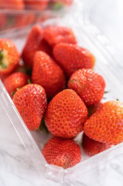 Taze çilekler, mutfak tezgahında dinlenen ve yıkanmaya, yenmeye ya da saklanmaya hazır orijinal plastik konteynerlerinde sergilenir..
