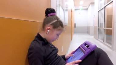 Sessiz bir koridora yerleşmiş bu genç artistik patinajcı, yaklaşan performansına zihinsel olarak hazırlanırken kendini tabletine kaptırmış bir sükunet anı buluyor..
