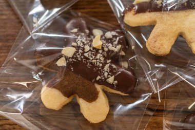 Dikkatlice paketlenmiş Noel kurabiyeleri, çikolataya batırılmış ve şeffaf selofan ambalajla sunulmuş, bayram hediyesi olarak mükemmel..