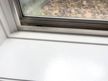 Bodrum penceresinin yakın plan görüntüsü beyaz iç pencere çerçevesini gösteriyor. Metal bir pencerenin dış görünüşü ise küçük taşlarla kaplı. Temiz pencere çerçevesi ve iyi korunmuş çerçeve