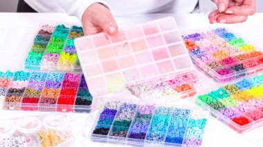 Kadın elleri şeffaf organizatörlerin renklerine göre sıralanmış boncuk koleksiyonunun üzerinde zarif bir şekilde duruyor. Boncuk dizisi, derin morlardan parlak portakallara kadar, titizlikle geniş bir yelpazeyi kapsıyor.