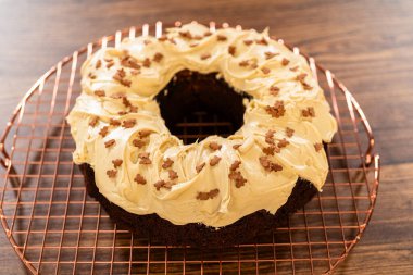 A gingerbread bundt cake being generously frosted with salted caramel frosting and topped with delightful gingerbread sprinkles. clipart