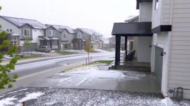 Castle Rock, Colorado, ABD-9 Haziran 2024-Ağır çekim-A varoş mahallesi modern evler fırtınadan sonra dolu tabakasıyla kaplandı. Olay yerinde park etmiş bir araba ve cadde var.