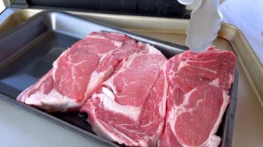 Bu resim barbekü ızgarasında pişen üç kalın bifteği, yukarıdaki koçanda folyoya sarılı mısırla birlikte, tipik bir açık hava yemek sahnesini görüntülüyor.