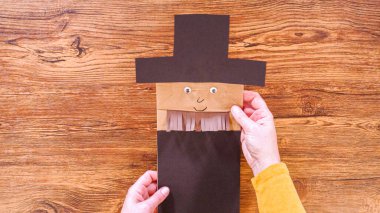 Adım adım. Düz yatıyordu. Öğretmen, kahverengi bir çantadan kağıt bir kukla yaparak, çalışma alanı olarak ahşap bir yüzey kullanarak çevrimiçi sınıfa rehberlik ediyor..