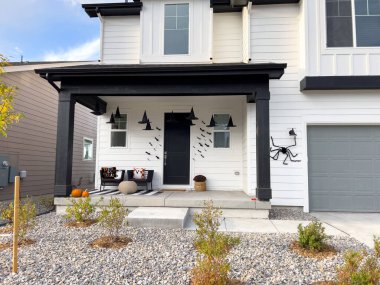 Castle Rock, Colorado, USA-October 12, 2024-A modern home with a decorated front porch for Halloween, featuring bats on the wall, pumpkins, and themed cushions. The house has a black-and-white clipart