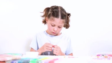 Genç kız derinden bilezik yapma sanatına odaklanmış. Canlı kil boncukları eşsiz kalıplara döküyor. Çalışma alanı çeşitli boncuklarla düzenlenmiş. Bu da nişanını gösteriyor.