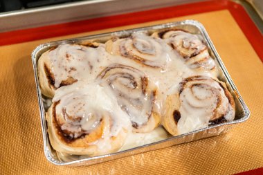 Fırından yeni çıkmış, tarçınlı çörek silikon bir hasırın üzerinde serinliyor, kremaları mutfak ışıklarının altında parlıyor..