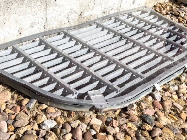 Üzerine özel pleksiglas takılmış bir bodrum penceresinin yakın çekim görüntüsü. Kapak pencerenin üzerinde güvenle duruyor. Etrafı dekoratif kayalarla çevrili. Korunma sağlıyor.