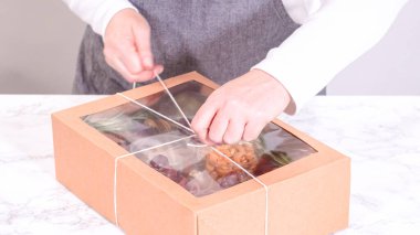 Elleri titizlikle bir kaseye taze kırmızı üzüm ekliyor, çeşitli peynirler, zeytinler ve pişirilmiş etlerle dolu güzel bir şarküteri kutusunu tamamlıyor.