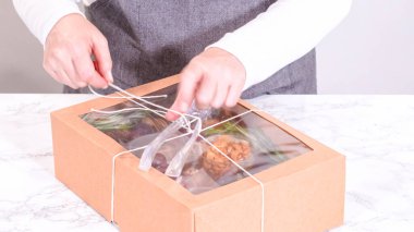 Elleri titizlikle bir kaseye taze kırmızı üzüm ekliyor, çeşitli peynirler, zeytinler ve pişirilmiş etlerle dolu güzel bir şarküteri kutusunu tamamlıyor.