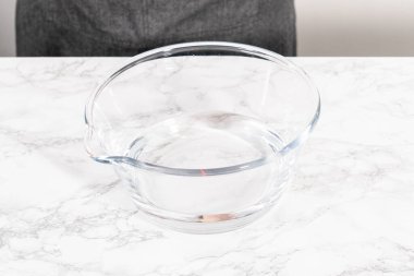 İçi su dolu geniş bir cam karıştırma kabı olgun çilekleri nazikçe temizlemek için hazır bekliyor. Kurumadan ya da depolamadan önce el değmemiş olduklarından emin olmak için..