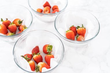 Parlak kırmızı çilekler, küf izleriyle karışmış, beyaz peçetedeki kağıt havluyla kaplı cam bir kasede dinleniyor, depolama tekniklerini gösteriyor..