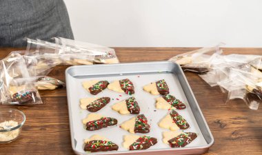 Dikkatlice paketlenmiş Noel kurabiyeleri, çikolataya batırılmış ve şeffaf selofan ambalajla sunulmuş, bayram hediyesi olarak mükemmel..