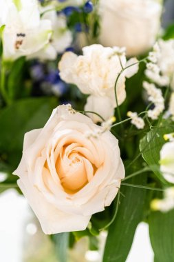 Taze beyaz güllerin ve çeşitli çiçeklerin bulunduğu büyüleyici bir buket, zarif bir vazoda düzenlenmiş, zamansız bir güzellik yayıyor..