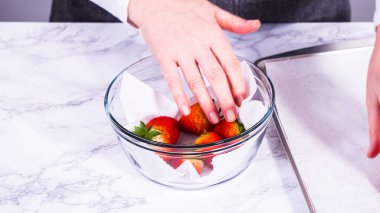 Çilekler, yeni yıkanmış ve kurutulmuş, cam bir kasede güzelce depolanmış kağıt havluyla kaplanmış ve tazeliği korumak için plastikle kaplanmış..