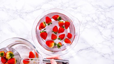 Düz yatıyordu. Olgun çilekler, depolama veya tüketimden önce temizlik ve uzun ömürlü olmak için meyveyi yıkamada bir adım olarak büyük bir bardakta karıştırma kabında suya gömülür..