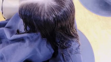 Nazik eller saç kurutma makinesini yeni kesilmiş genç bir kızın üzerinden geçirir ve titiz bir şekilde kestikten sonra kurutma işlemini gösterir. Kurutucunun sıcaklığı onun kilitlerine hayat veriyor.