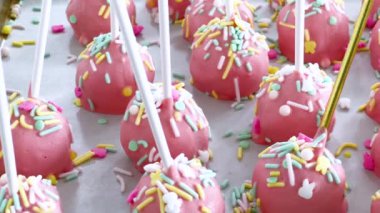 Parşömen kağıdına güzelce yerleştirilmiş, bu elle batırılmış pembe kek parçaları, tatlı zevklere şenlikli bir dokunuş katan bir gökkuşağı süslemesi ile süslenmiş, eğlenceli bir ikram.