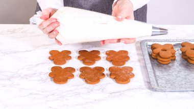 Gingerbread cookies await their second halves on a marble surface, each meticulously piped with buttercream to craft delightful sandwich treats. The precision of the piping adds a festive touch. clipart