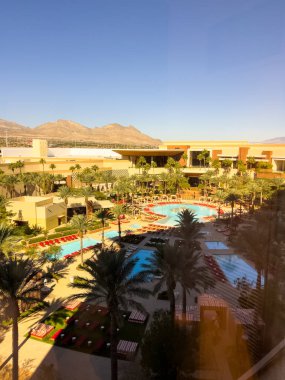 Las Vegas, Nevada, ABD-08 Kasım 2024 Las Vegas 'taki Red Rock Resort' un lüks havuz manzarası, uzun palmiye ağaçları ve canlı kırmızı şezlonglar tarafından çerçevelenmiş. Sakin mavi havuzlar ve