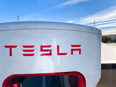 Mesquite, Nevada, ABD-10 Kasım 2024 - Tesla Cybertruck 'ın bir Tesla Superşarj istasyonuna bağlı yan görüntüsü, açık mavi gökyüzü altında aracın parlak tasarımını gösteriyor. Palmiye ağaçları ve yakınlarda